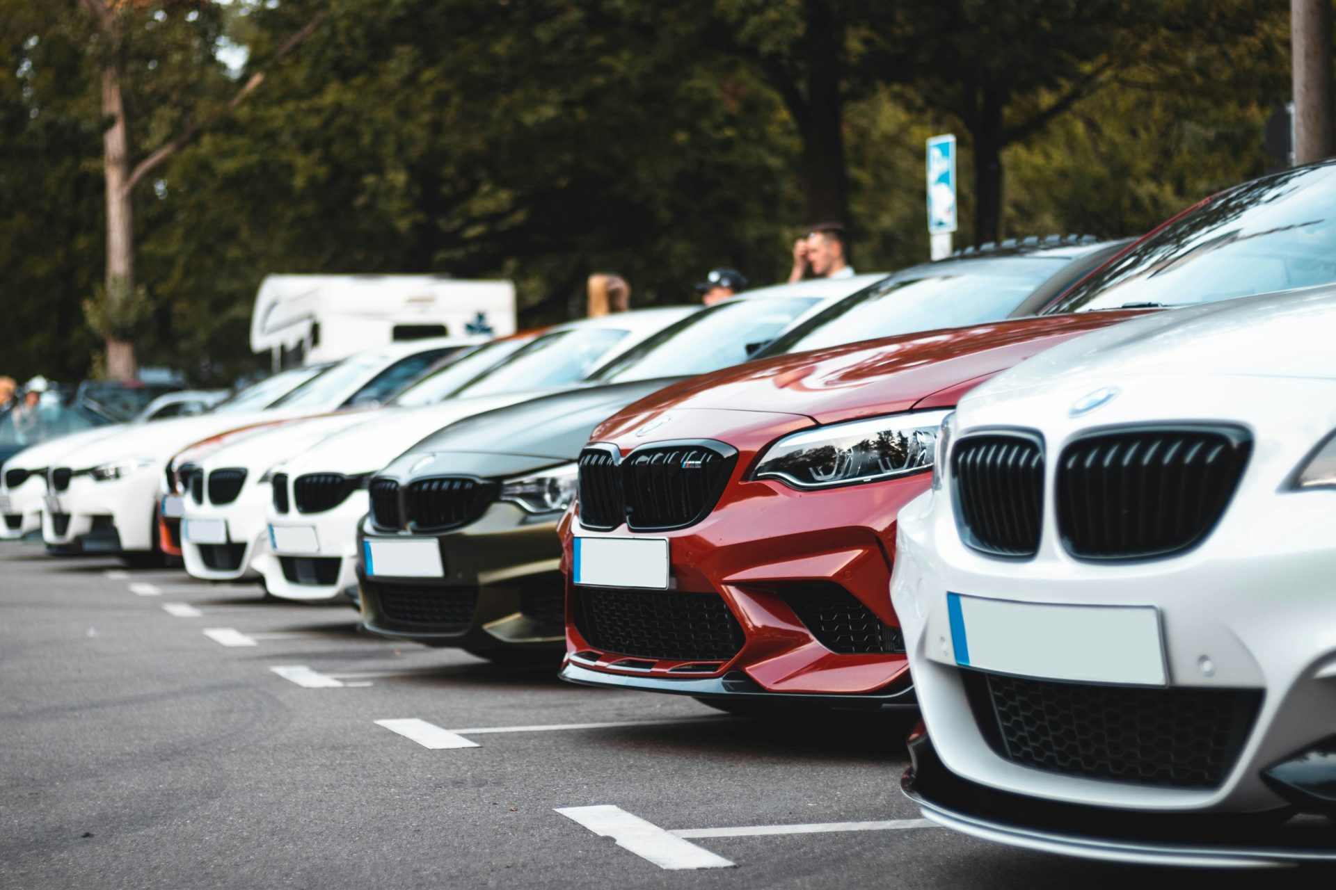 A row of parked cars including white, olive, and red sedans in a lot